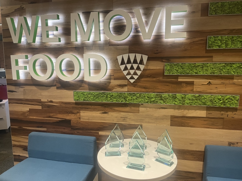 A group of trophies sit on a table in front of a wall decorated with the words We Move Food